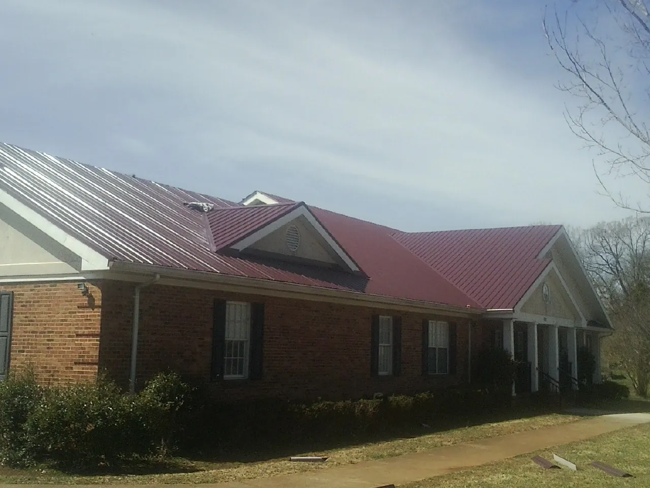 Red metal roof with gabled entries on a long brick building, from a Hail Damage Roof Repair job in Richwood