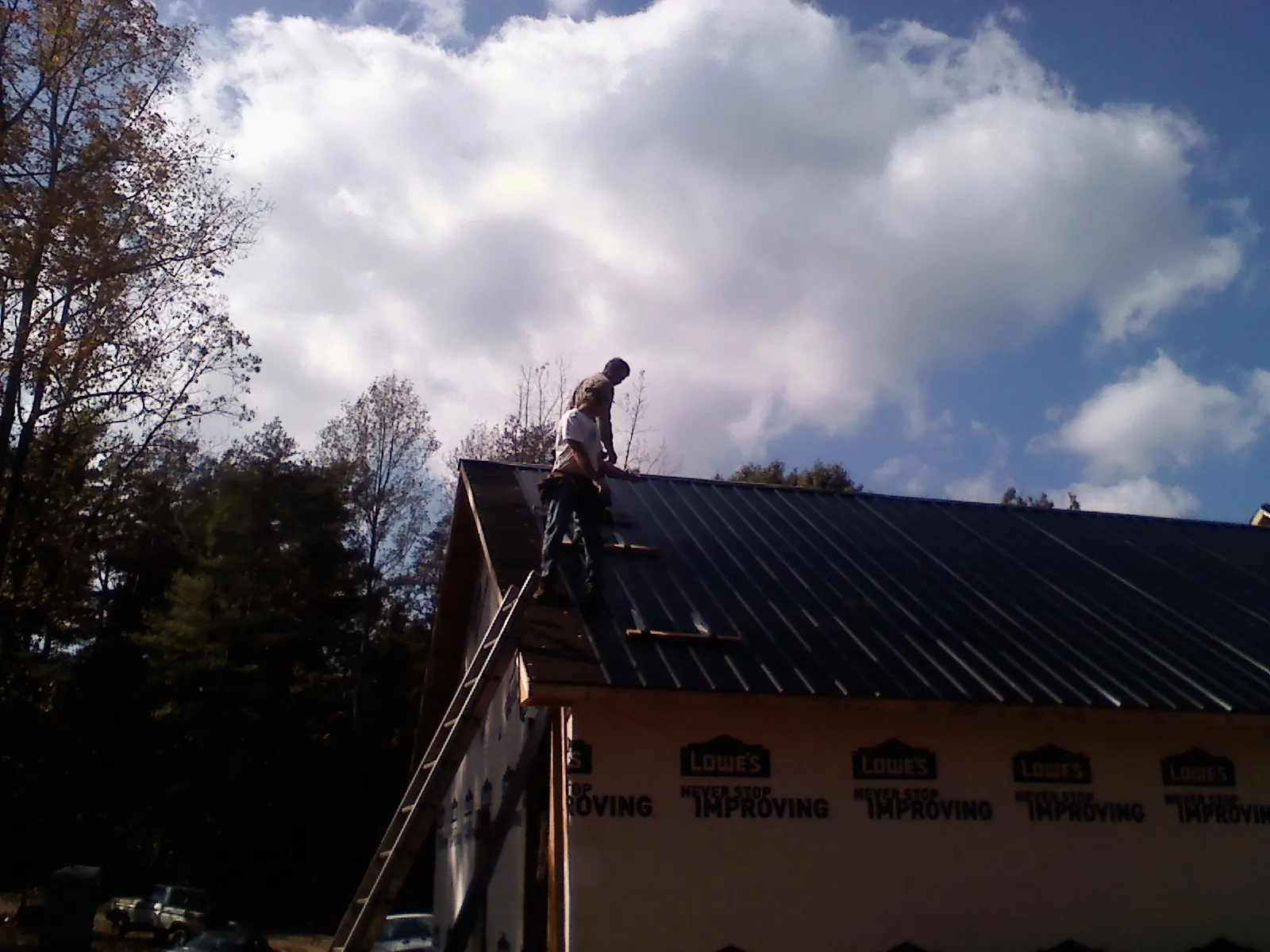 Roofer fastening dark metal panels high against a cloudy sky, from a Roof Inspection job in Richwood